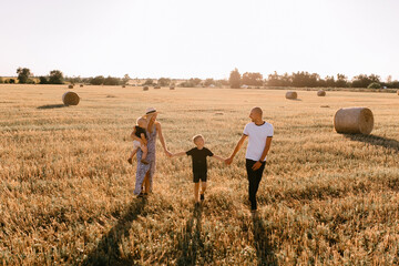 happy family walks in the field near the haystack at sunset, mom dad and two sons, the family is happy with smiles on their faces, hug the children