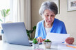 Elderly woman reads a bank loan notice or letter - Grandmother works from home with laptop and paperwork - Planning budget and retirement benefits and managing finances