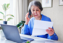 An Elderly Woman Pays Taxes Or Other Bills Online - A Pensioner Calls On The Phone And Finds Out Information About A Loan Or Her Savings - Online Help Concept For The Elderly