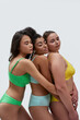 © Svitlana - Three multiethnic young women with different body types in colorful underwear embracing each other while posing together with eyes closed isolated over white background