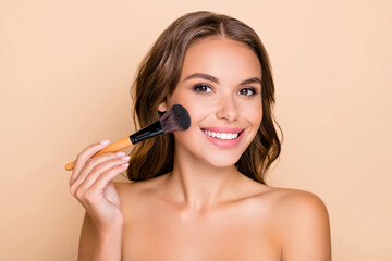 photo of young happy smiling beautiful woman doing contouring apply blush on cheeks isolated on beig