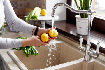 Close-up of a girl s hands washing a lemon in the sink in a home kitchen. The concept of health and a healthy lifestyle. Healthy eating, diet, vegetarianism