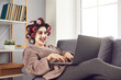 © Studio Romantic - Funny crazy cheerful woman distant worker in curlers and cosmetics mask on face sitting on sofa and working online at laptop from home. Funny women working at home concept