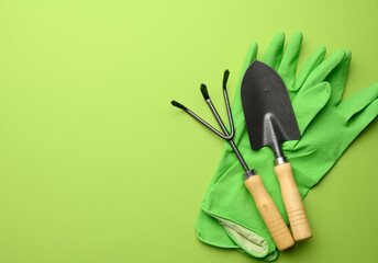 Wall Mural - green rubber gloves and garden set of shovels, rakes, pitchforks on a green background