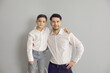 © Studio Romantic - Positive father and son in stylish white shirts and jeans standing hugging and looking at camera over grey wall background. Happy fatherhood, childhood, family concept