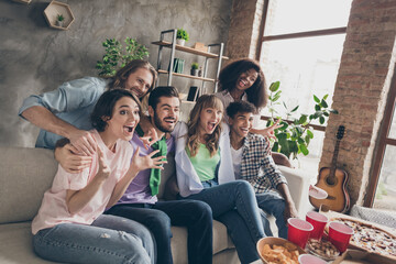 Poster - Portrait of attractive overjoyed cheerful friends gathering sitting on sofa having fun watching film in house brick loft style indoors