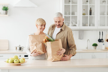 ordering food online. senior couple arriving from supermarket with grocery bag and unpacking in kitc