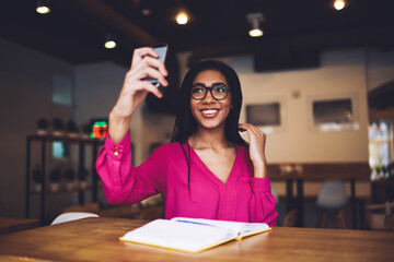 Wall Mural - Cheerful African American woman taking selfie on smartphone