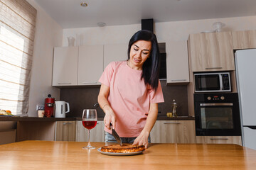 Wall Mural - young smiling dark-haired woman cuts a homemade pie in the kitchen. Cooking breakfast