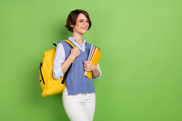 Poster - Photo portrait of female student with yellow rucksack keeping book stack looking copyspace isolated bright green color background