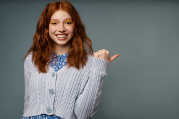 Wall Mural - Young ginger happy woman smiling and pointing finger aside