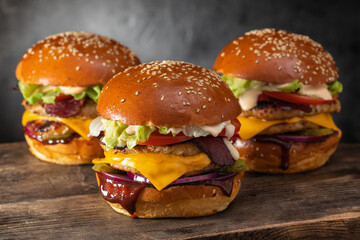 Wall Mural - Three yummy juicy hamburgers with double cutlet and cheese on a wooden table. Grilled chicken burger.