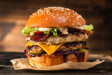 Grilled chicken burger with double cutlet, cheese and vegetables on a wooden table. Grilled cheeseburger. Fast food takeaway.