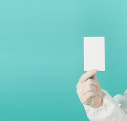 Wall Mural - Hand holding empty blank white card.Hand with ppe suit, latex glove on green or Tiffany Blue background. Empty space for text