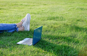 Laptop and legs on green grass. Freelance concept, work or study outdoors. Copy space