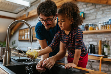 Multiracial father and daughter washing dishes in the kitchen