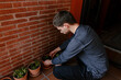 © Edgar - Hombre joven caucásico dejando un planta dentro de su maceta en el suelo junto a otras plantas en la terraza de su casa