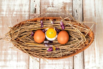 Easter eggs on straw in a wicker basket on an old wooden table surface. Easter celebration concept.