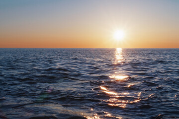 The setting sun goes into the sea on the horizon with a light track and reflections on the sea.