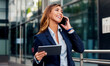 © bobex73 - Businesswoman holding tablet and making a phone call in front of the corporation. Business, lifestyle concept