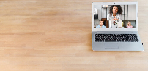 Wall Mural - Video meeting concept. Laptop on the wooden table with empty space for advertisement, group of people from laptop screen video calling having virtual meeting, using app for distance communication