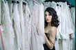 © Alex Li - Beautiful girl in black dress, hiding behind white dresses hanging on a hanger. Sensual look right at the camera.