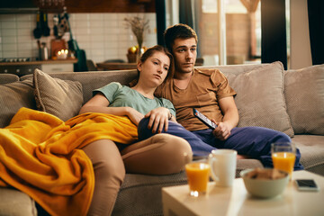 Wall Mural - Young couple watching movie on TV while relaxing at home.