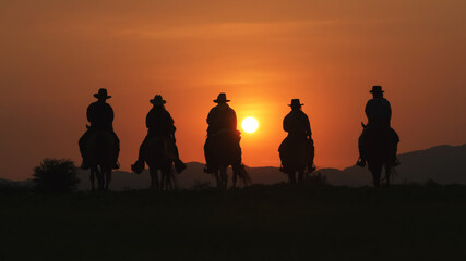 vintage and silhouettes of a group of cowboys sitting on horseback at sunset.