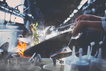 Wall Mural - Chef stir fry busy cooking in kitchen. Chef stir fry the food in a frying pan, smoke and splatter the sauce in the kitchen.