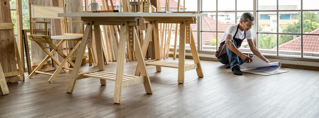 Aged Asian joiner working with blueprint on floor