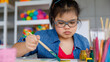 © Bangkok Click Studio - Young Asian down syndrome little girl sitting at desk with colors and painting with concentrated and calm. painting. Concept for education for disabled kid.