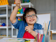 © Bangkok Click Studio - From above happy Asian girl with Down syndrome smiling and showing green gouache to camera in art classroom
