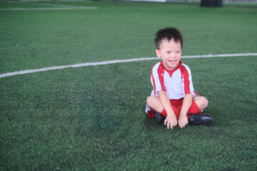 Cute little smiling Asian kindergarten kid, football player in soccer uniform is playing football at Training Session, Soccer Drills for Kids