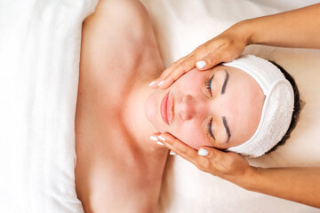 Wall Mural - Cosmetologist makes a woman a facial massage procedure. Portrait of the client and the doctor's hands in close-up. Copy space. Top view. Concept of cosmetology and treatment