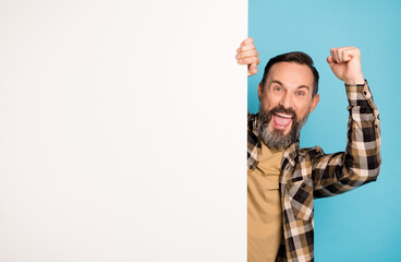 Photo of guy raise fist open mouth hold white card empty space wear checkered shirt isolated blue background