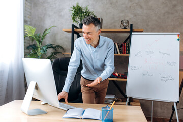 Confident caucasian businessman in the office. Adult business leader in formal wear conducts online briefing or presentation for colleagues using computer, shows financial strategy on flipchart