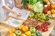 Cropped dietitian, nutritionist or doctor standing by desk writing about benefits of eating fresh fruit and vegetables