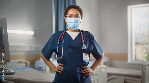 Hospital Ward: Portrait of Posing Professional Black Female Head Nurse, Doctor, Surgeon Wearing Face Mask Looks at Camera. Modern Clinic with Advanced Equipment and Professional Staff