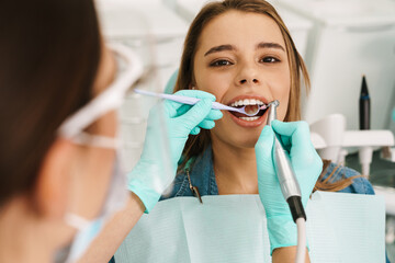 Wall Mural - Woman sitting in medical chair while dentist fixing her teeth