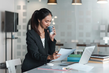 Wall Mural - Asian businesswoman sitting looking at document with drinking coffee at the office.