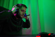© snedorez - Gamer or streamer in headphones with microphone sits at home in neon light and plays at pc