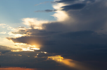 Wall Mural - dramatic dark sky with rays and white clouds at sunset