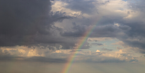 Wall Mural - rainbow on dramatic dark sky with rays and white clouds