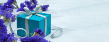 A Blue Box With A Gray Ribbon. Gift Wrap And Blue Flowers.