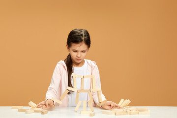 children plays with wooden constructor on desk.