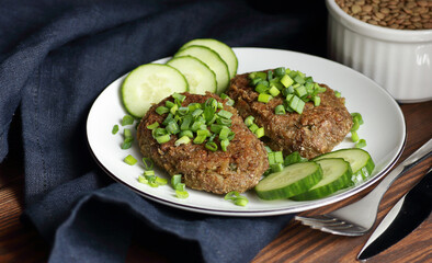 Wall Mural - Lentil cutlets garnished with green onions and cucumber on rustic wooden table, closeup, vegetarian lenten eastern dish, healthy vegan food concept