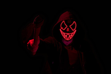 Man armed with an axe and wearing a scary lighting neon glow mask and a hoodie on black background.