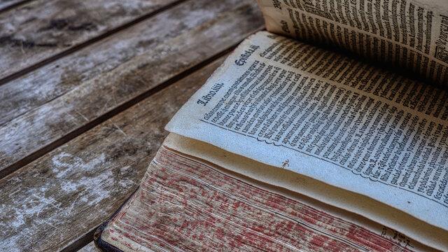 An old book on a wooden table. A 15th-century book written in spanish using the gothic script. Selective focus