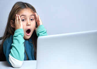 Shocked child girl with open mouth and bulging eyes looks at a computer laptop screen. Internet porn censorship concept, adult content 18+