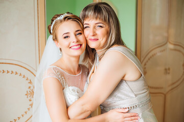 a beautiful bride in a wedding dress poses with her mother in the morning at home before the ceremon